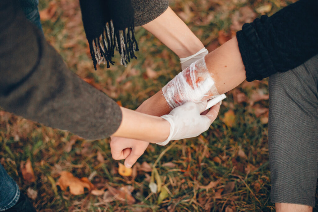 Providing first aid in the park. Man bandaged injured arm. Guy helps a friend.